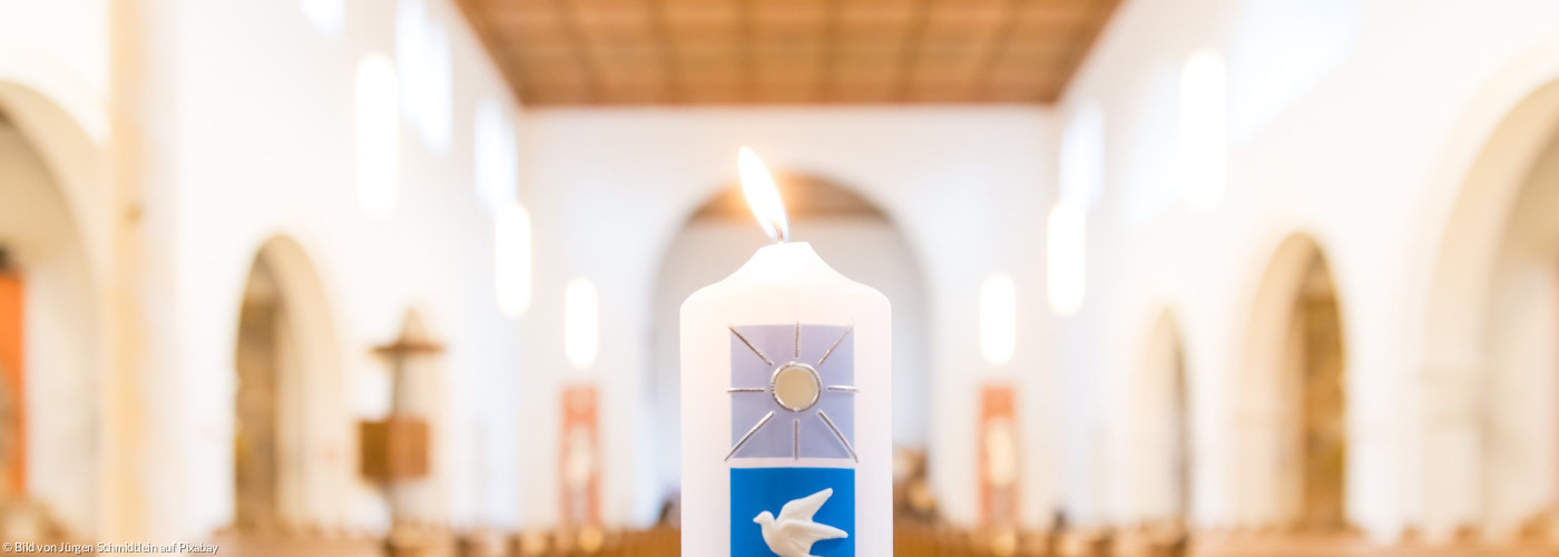 Taufkerze, im Hintergrund sieht man Kirchenbänke