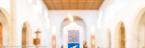 Taufkerze, im Hintergrund sieht man Kirchenbänke